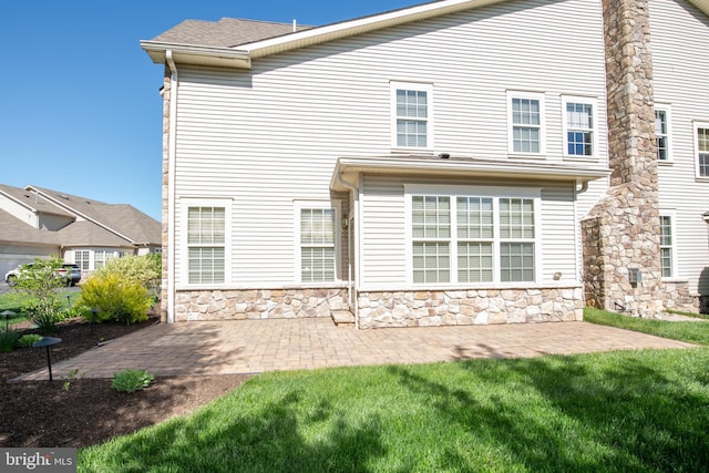 back of property featuring a lawn, stone siding, and a patio area