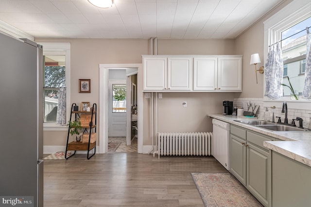 kitchen featuring white dishwasher, a sink, light wood finished floors, light countertops, and radiator heating unit