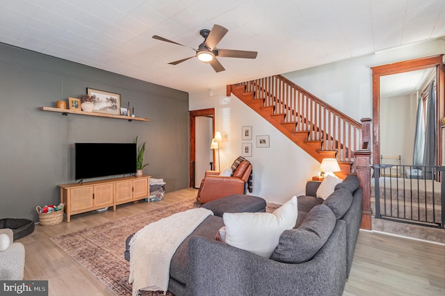 living area with ceiling fan, wood finished floors, and stairway