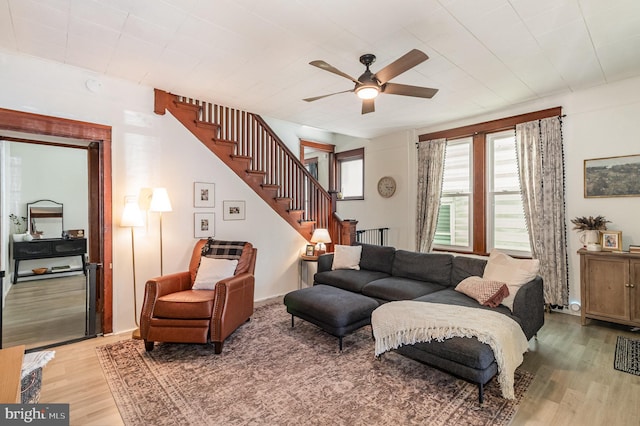 living area featuring light wood-style floors, ceiling fan, and stairway
