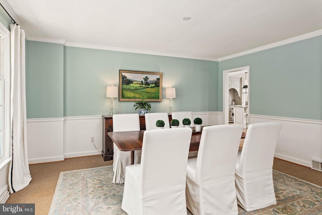 dining room featuring a wainscoted wall, ornamental molding, arched walkways, and visible vents