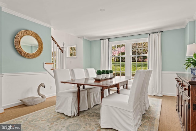 dining area with stairway, ornamental molding, light carpet, and wainscoting