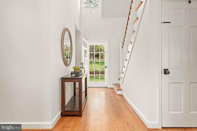 interior space with baseboards, stairs, light wood finished floors, and a towering ceiling