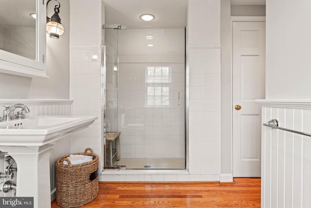 bathroom with a sink, a wainscoted wall, a shower stall, and wood finished floors