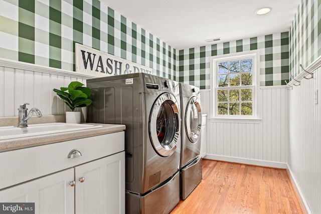 clothes washing area featuring light wood-style floors, cabinet space, washing machine and clothes dryer, and wallpapered walls