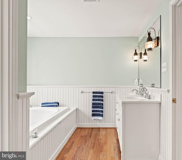 full bath with a garden tub, visible vents, wood finished floors, a wainscoted wall, and vanity