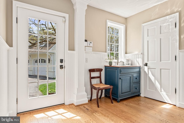 doorway with decorative columns, light wood-style flooring, visible vents, and a wainscoted wall