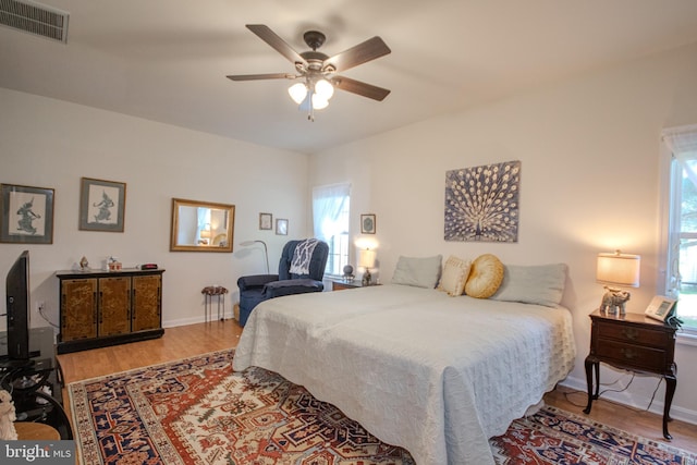 bedroom featuring ceiling fan, baseboards, visible vents, and wood finished floors