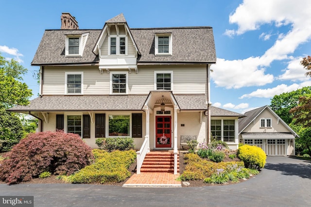 view of front of house featuring a shingled roof, an outdoor structure, a chimney, and driveway