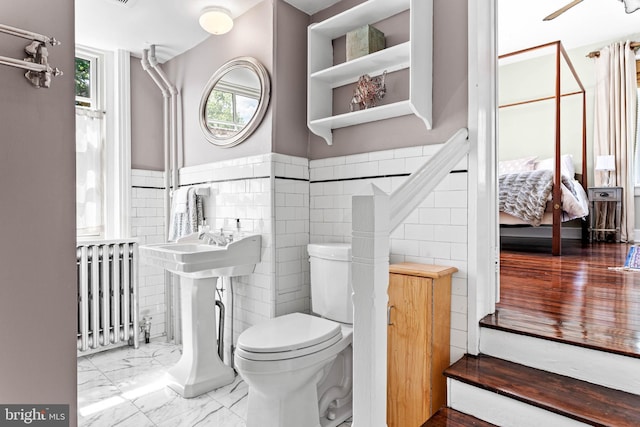 ensuite bathroom with radiator heating unit, toilet, tile walls, a wainscoted wall, and marble look tile flooring
