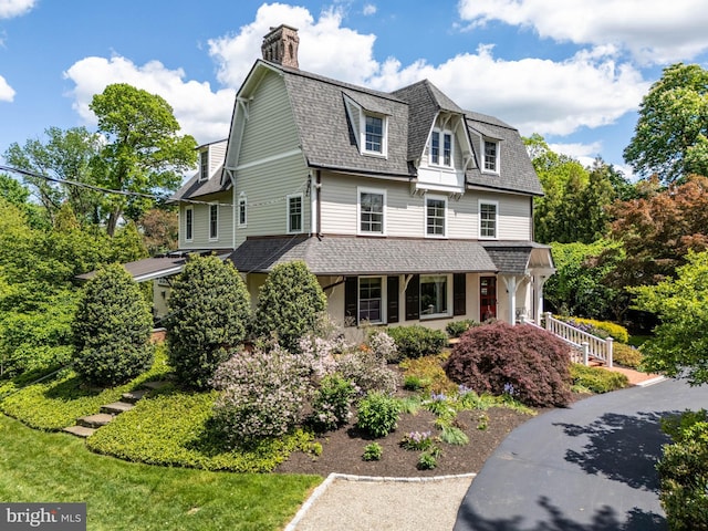 view of front of home featuring a shingled roof, a porch, a chimney, and a gambrel roof