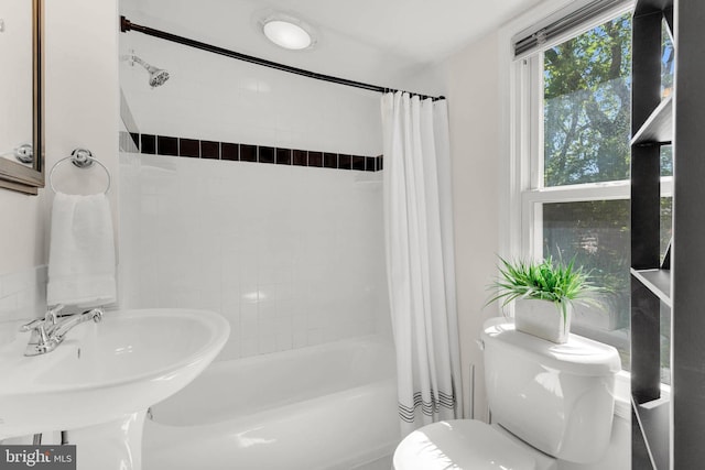 bathroom featuring a sink, shower / bathtub combination with curtain, and toilet