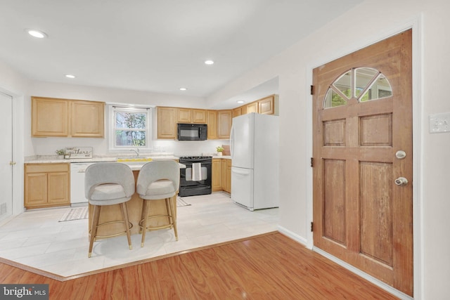 kitchen with a breakfast bar area, a center island, light countertops, a sink, and black appliances