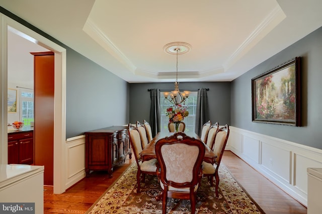 dining space featuring a tray ceiling, a chandelier, wood finished floors, ornamental molding, and a decorative wall
