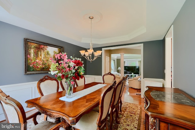 dining room featuring a raised ceiling, wood finished floors, decorative columns, wainscoting, and a decorative wall