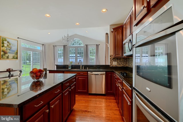 kitchen with stainless steel appliances, a sink, light wood finished floors, lofted ceiling, and a chandelier