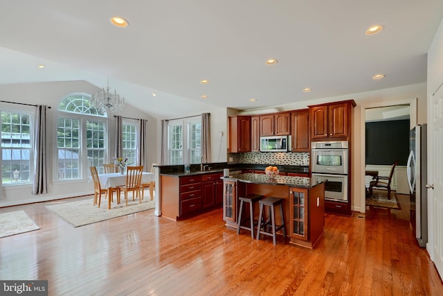 kitchen featuring stainless steel appliances, a kitchen island, lofted ceiling, light wood-style flooring, and a peninsula