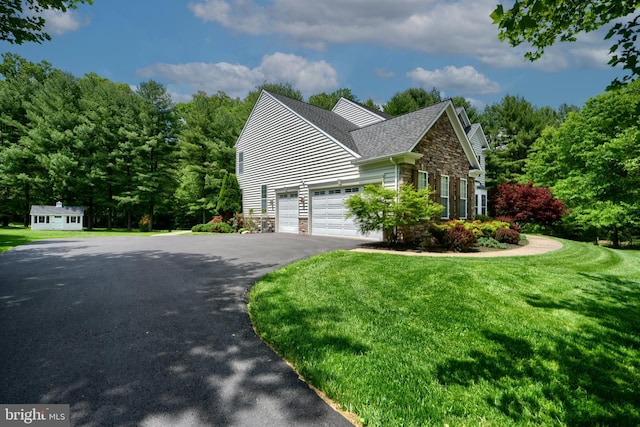 view of side of home featuring stone siding, a garage, a lawn, and asphalt driveway