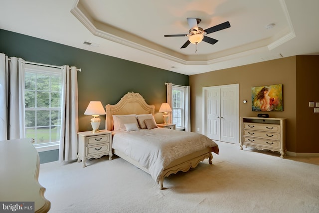 carpeted bedroom with a raised ceiling, a closet, and a ceiling fan