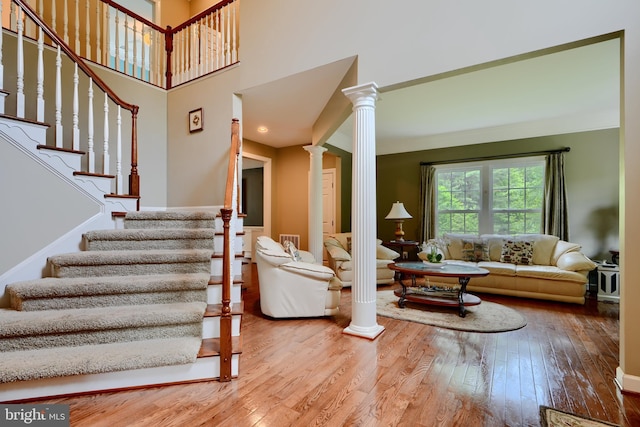 living area with decorative columns, wood-type flooring, and stairs