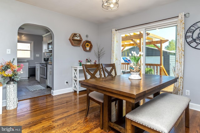 dining space with baseboards, wood finished floors, and arched walkways