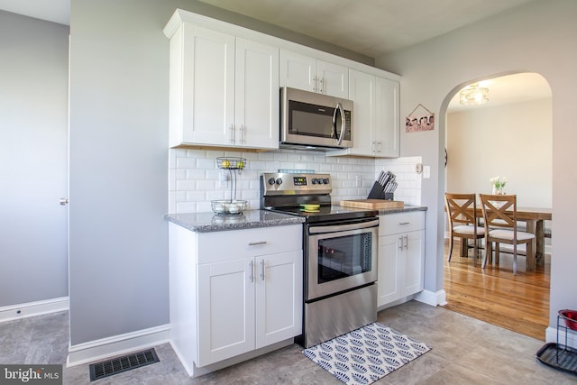 kitchen with tasteful backsplash, arched walkways, appliances with stainless steel finishes, white cabinets, and visible vents