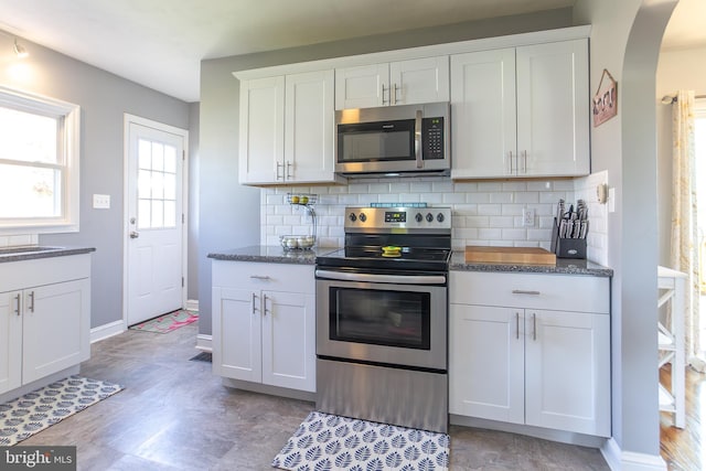 kitchen with white cabinets, arched walkways, backsplash, and appliances with stainless steel finishes