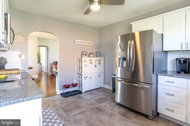 kitchen featuring arched walkways, decorative backsplash, stainless steel appliances, white cabinets, and a ceiling fan