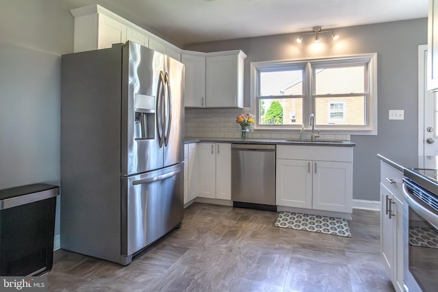 kitchen with a sink, backsplash, white cabinetry, dark countertops, and appliances with stainless steel finishes