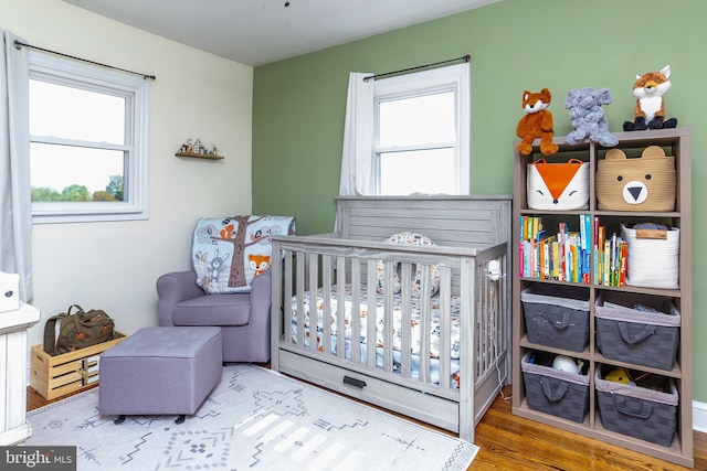 bedroom featuring a crib, wood finished floors, and multiple windows