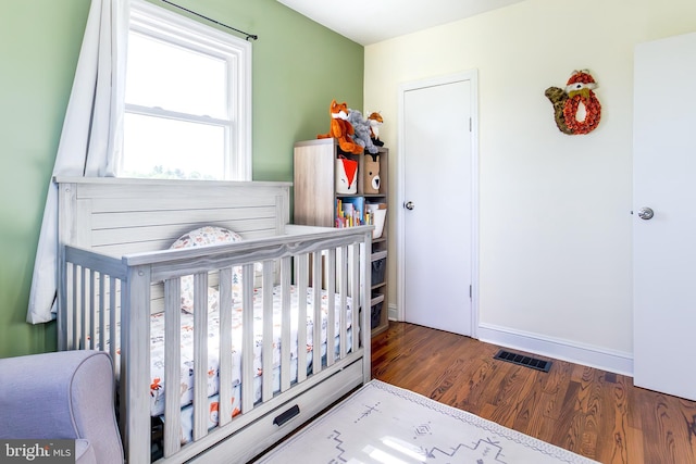 bedroom with a crib, visible vents, wood finished floors, and baseboards