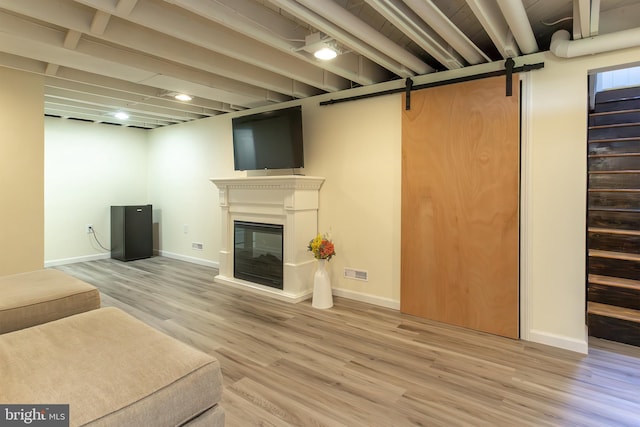 unfurnished living room featuring a barn door, a glass covered fireplace, visible vents, baseboards, and wood finished floors