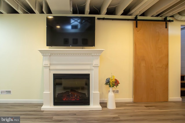 room details with wood finished floors, visible vents, a glass covered fireplace, and a barn door