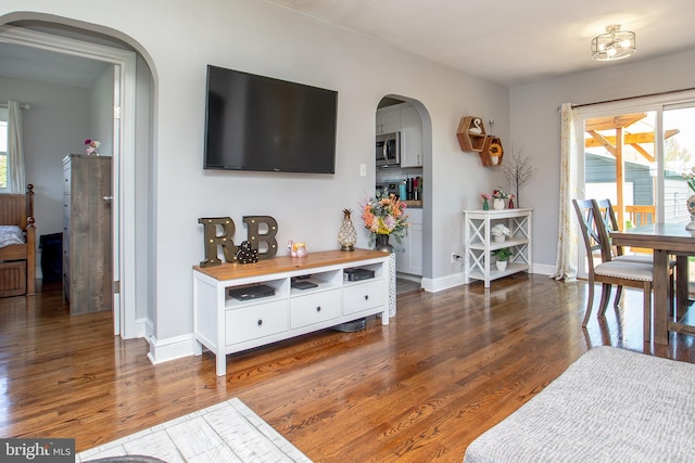 living area with arched walkways, a wealth of natural light, and wood finished floors
