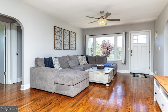living area with dark wood finished floors, baseboards, arched walkways, and a ceiling fan