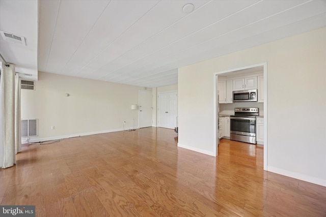 unfurnished living room featuring visible vents, light wood finished floors, and baseboards