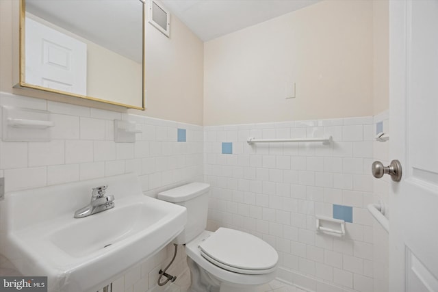 half bathroom with visible vents, tile walls, wainscoting, a sink, and toilet