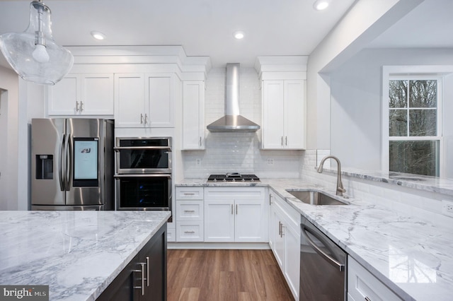 kitchen featuring wall chimney range hood, dark wood-style flooring, white cabinets, appliances with stainless steel finishes, and a sink