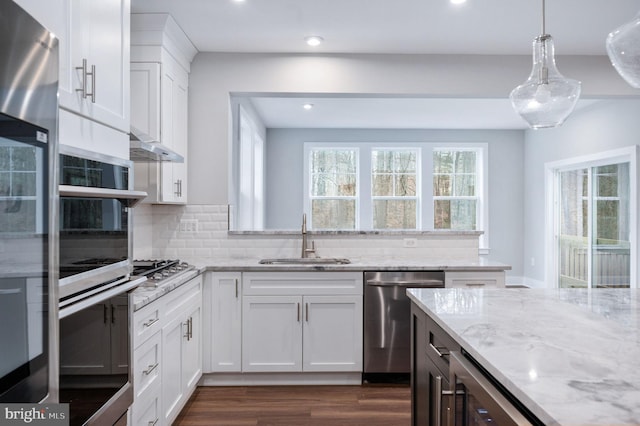 kitchen featuring white cabinetry, light stone counters, a sink, dark wood finished floors, and appliances with stainless steel finishes