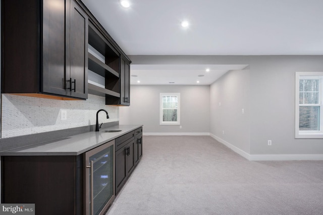 kitchen with a sink, baseboards, light countertops, beverage cooler, and light carpet