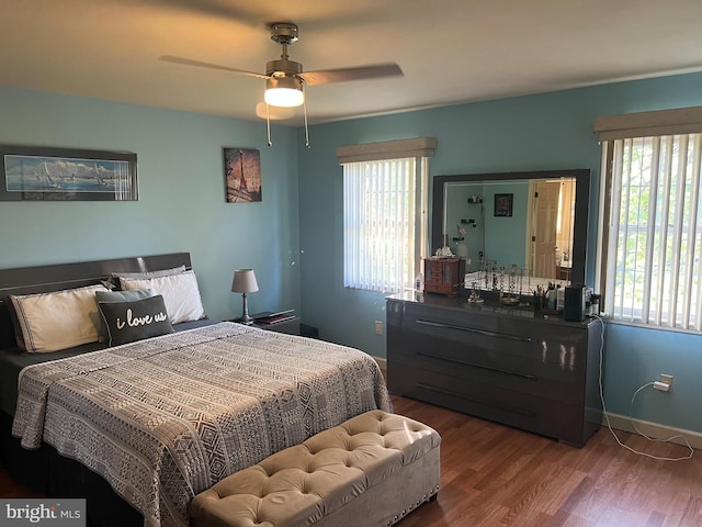 bedroom featuring a ceiling fan, baseboards, multiple windows, and wood finished floors