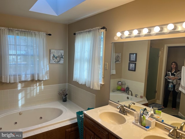 full bath featuring double vanity, a skylight, a tub with jets, and a sink