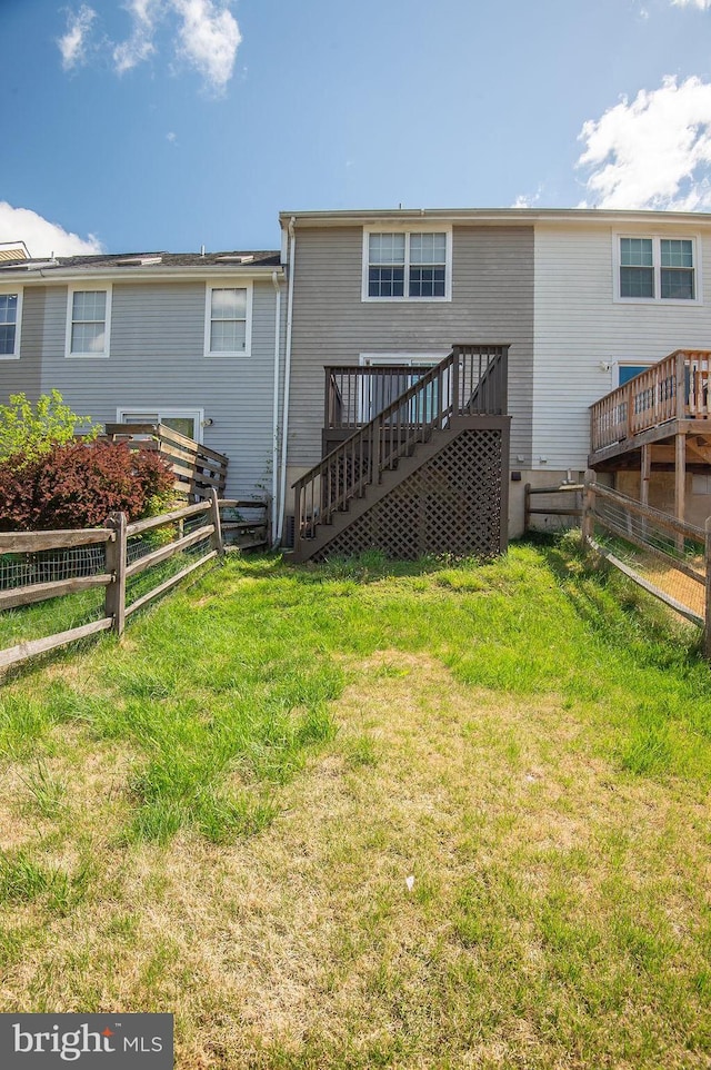 back of property featuring a lawn, fence, a wooden deck, and stairs