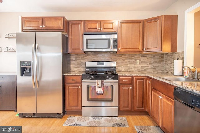 kitchen featuring decorative backsplash, a sink, light wood-style floors, stainless steel appliances, and light stone countertops