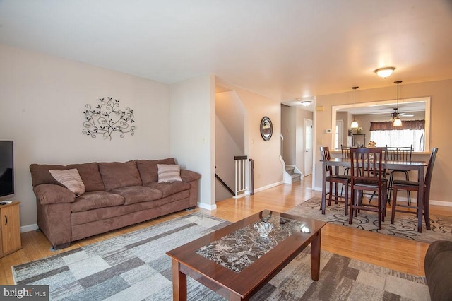 living area with a ceiling fan, stairway, wood finished floors, and baseboards