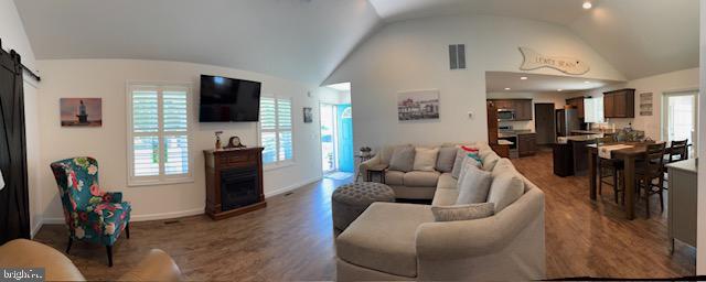 living room with visible vents, dark wood finished floors, a barn door, baseboards, and lofted ceiling