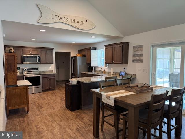 kitchen featuring a peninsula, wood finished floors, lofted ceiling, dark brown cabinets, and stainless steel appliances