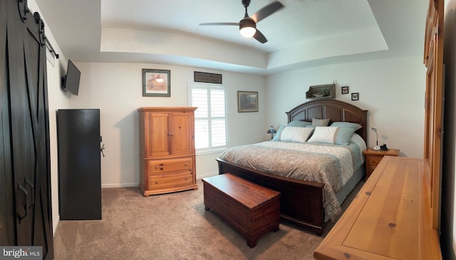 bedroom with ceiling fan, light colored carpet, a barn door, baseboards, and a tray ceiling