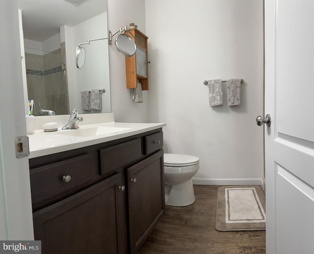 bathroom with vanity, wood finished floors, toilet, baseboards, and a tile shower