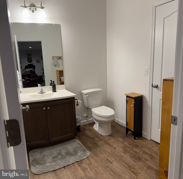 ensuite bathroom with wood finished floors, vanity, baseboards, toilet, and connected bathroom